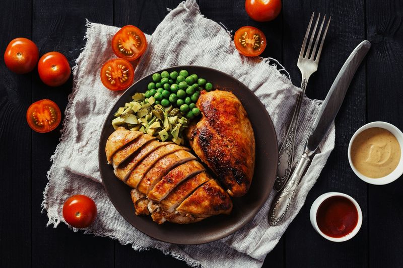 A plate of grilled chicken, peas and vegetables