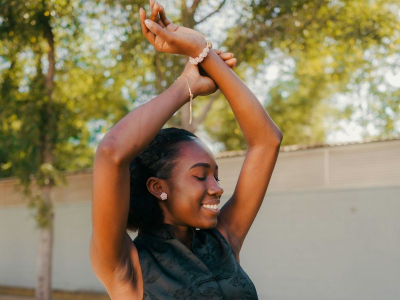A woman smiling as she stretches her arms overhead outdoors